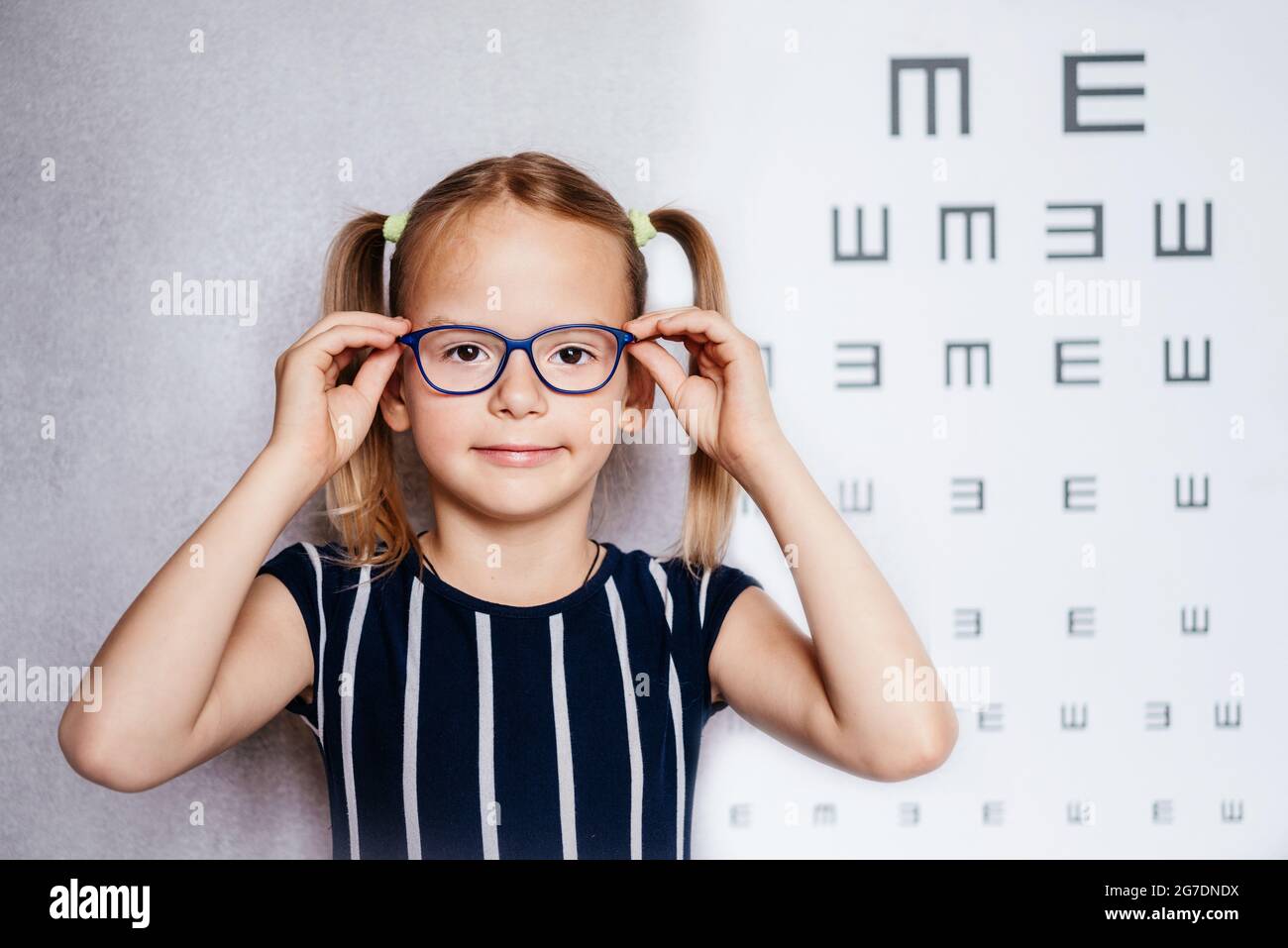 Happy little girl wearing glasses taking eyesight test before school