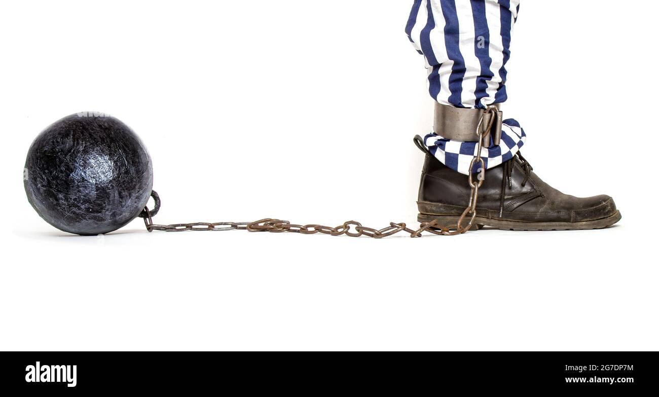 a leg of a prisoner in striped pants and a rough boot chained with an iron ball with shackles in profile Stock Photo