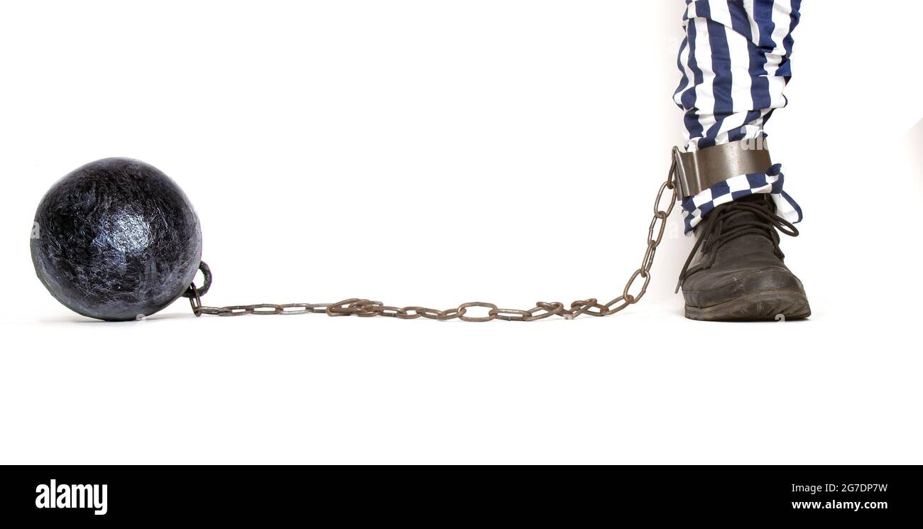 a leg of a prisoner in striped pants and a rough boot chained with an iron ball with shackles in front Stock Photo