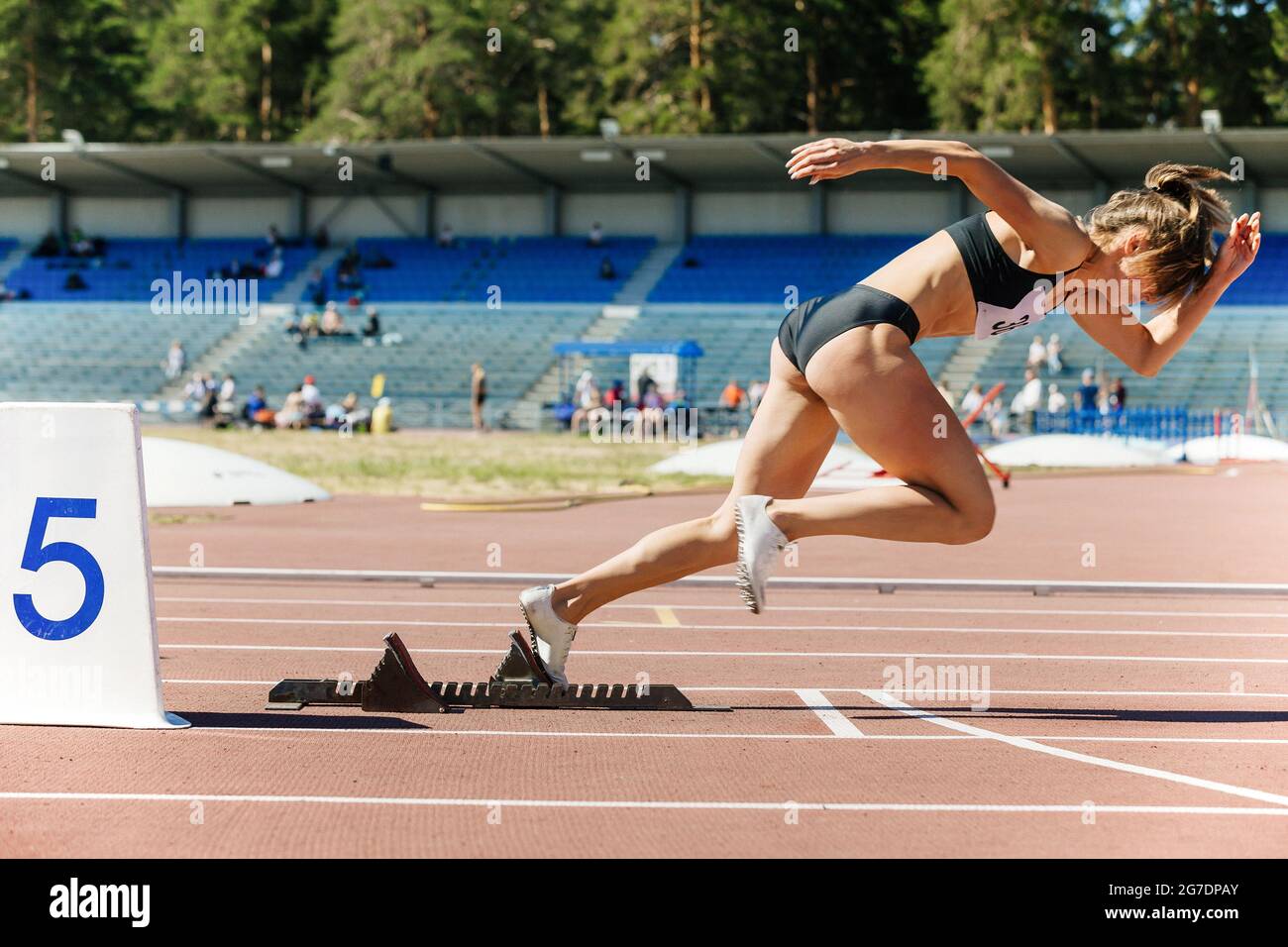 girl runner sprinter running from starting blocks to competition Stock Photo