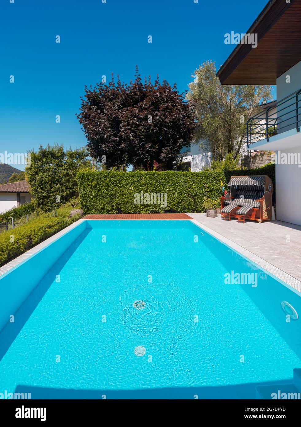Front view pool with clear water and large green hedge, perfect for a vacation. Sunny day with blue skies and nobody inside. Stock Photo