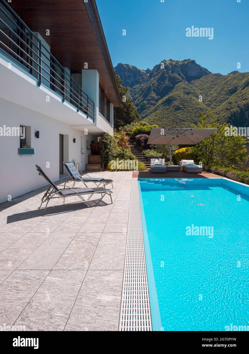 Modern two-story house with large pool overlooking the mountains. Two chaise lounges to enjoy the sun, two sunbeds and a large open umbrella to enjoy Stock Photo