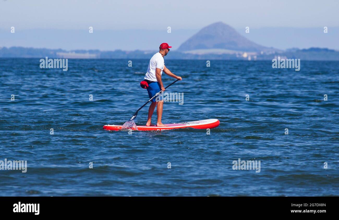 Portobello, Edinburgh, Scotland, UK weather. 13h July 2021. Hot and sunny afternoon at the seaside.Temperature of just over 22 degrees centigrade. Pictured: skilful paddleboard enjoying a splash on the Firth of Forth with Berwick Law. Credit: Scottishcreative/ Alamy Live News. Stock Photo