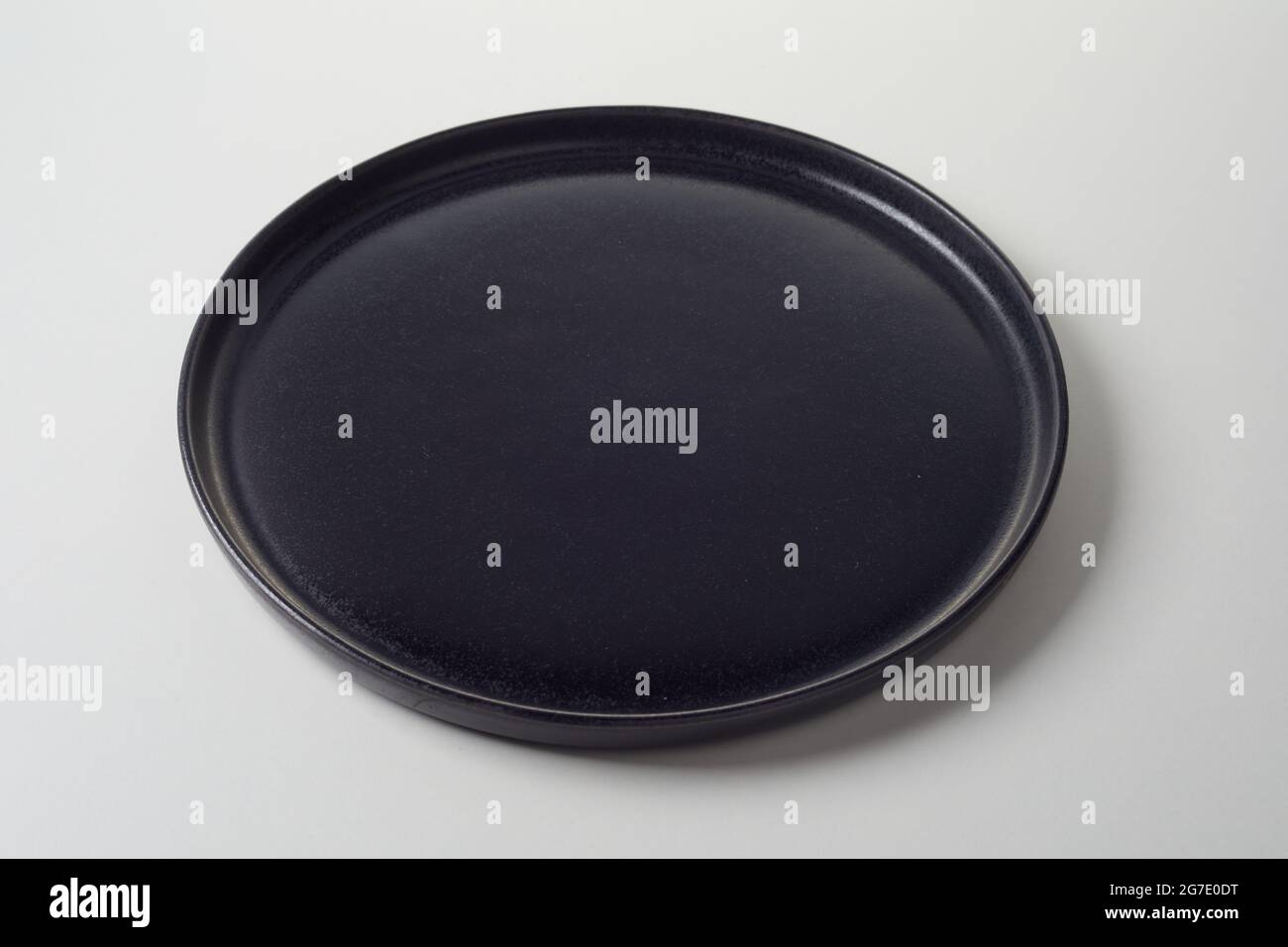 Circular clean black empty plate with raised rim ready for food placement for advertising on a white studio background in a high angle view Stock Photo