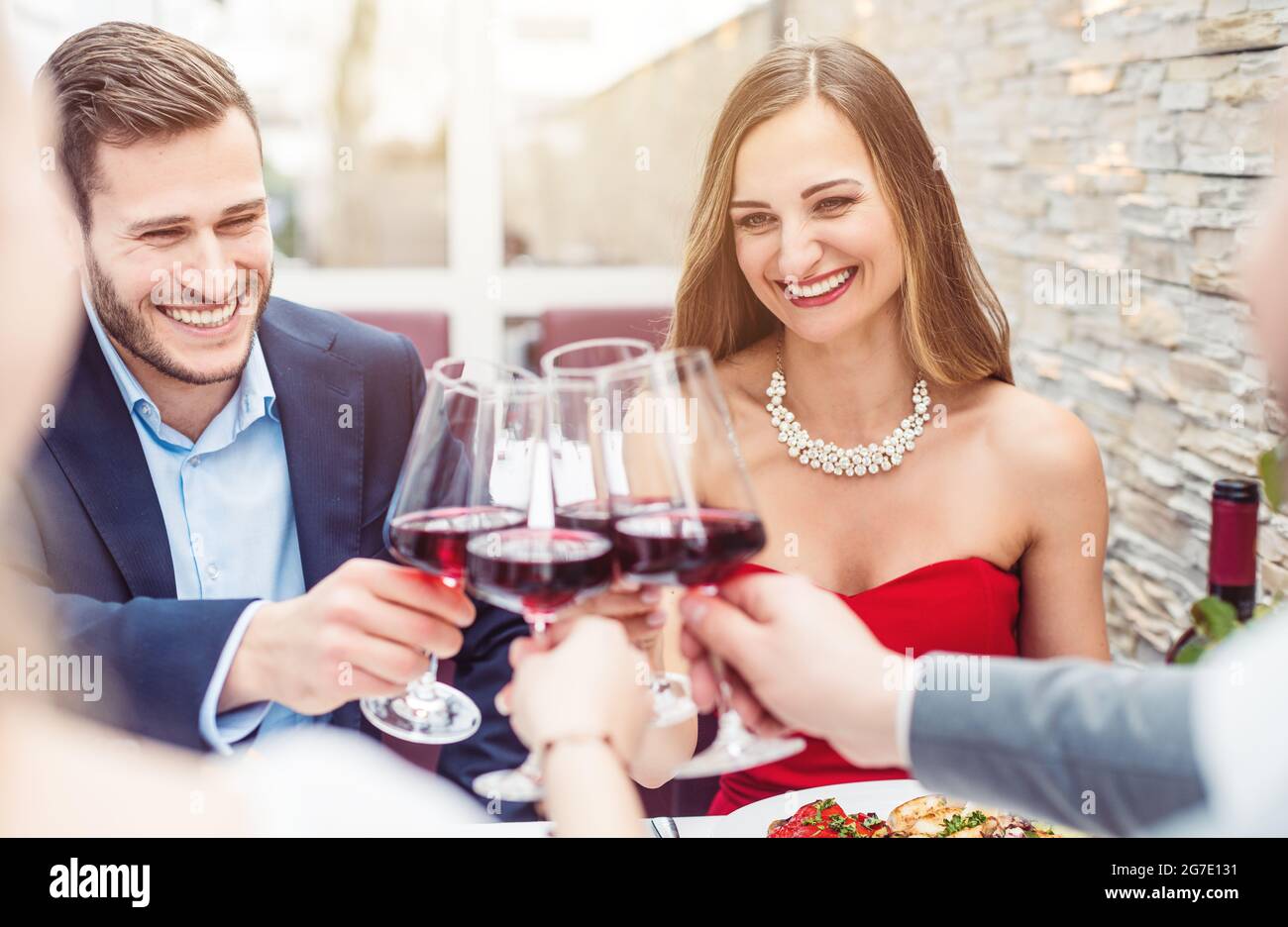 Group of cheerful people sitting on restaurant table toasting with red wine Stock Photo