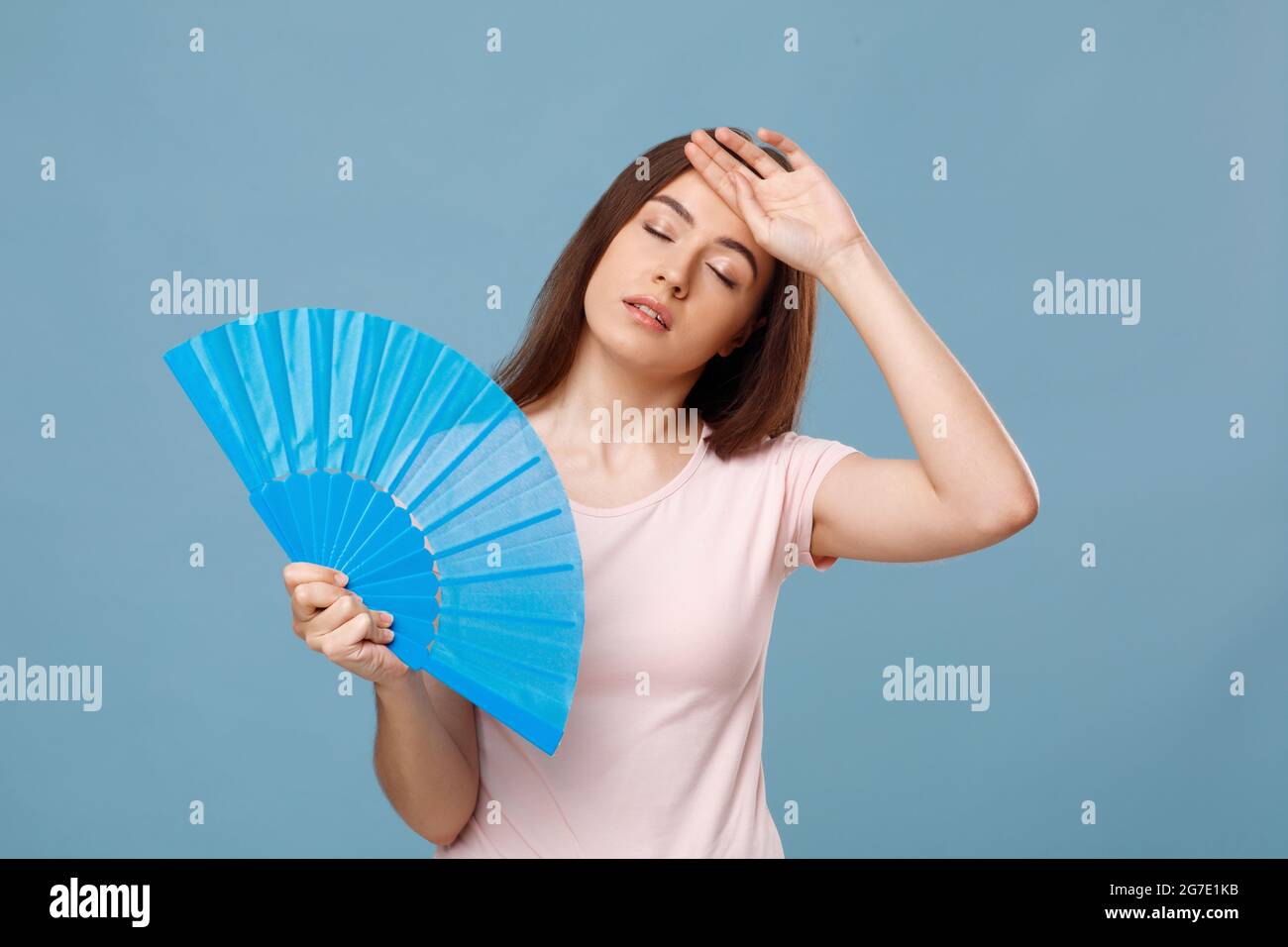 Exhausted caucasian young woman with fan touching her forehead Stock Photo