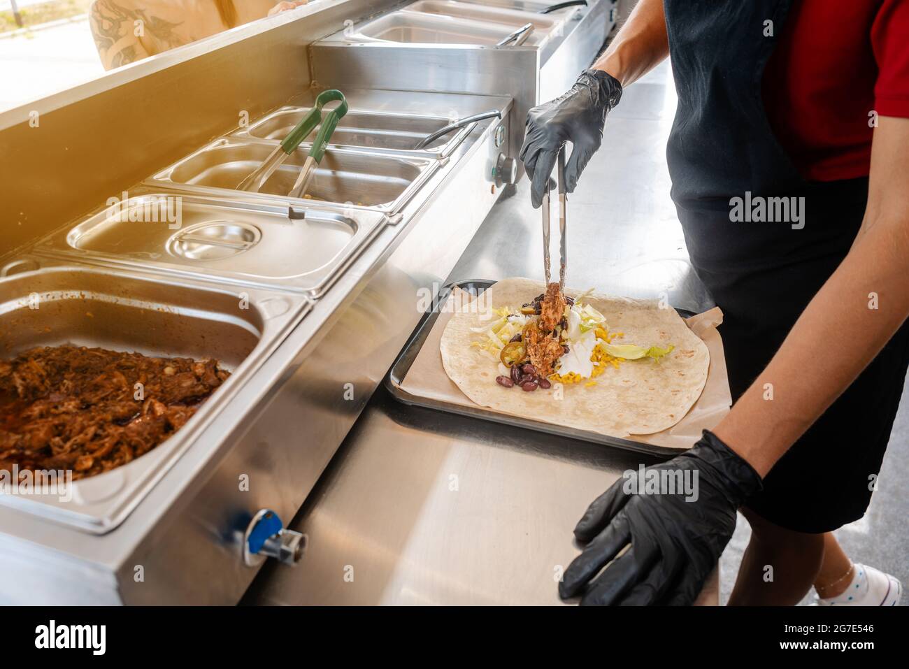 Woman preparing burrito in a food truck putting the ingredients in