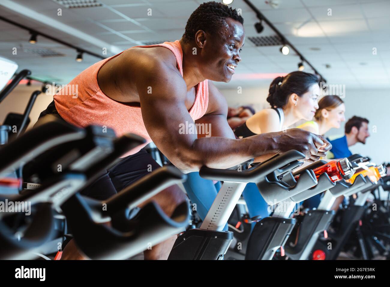 African man and friends exercising on fitness bike in gym Stock Photo