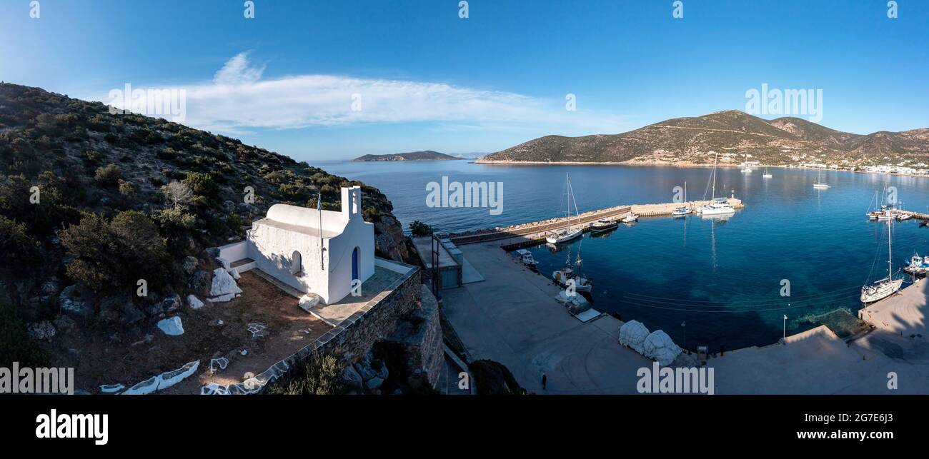Sifnos island, Platis gialos aerial drone view. Greece Cyclades. Small church on a hill, boats moored at the marina, calm Aegean Sea, blue sky backgro Stock Photo