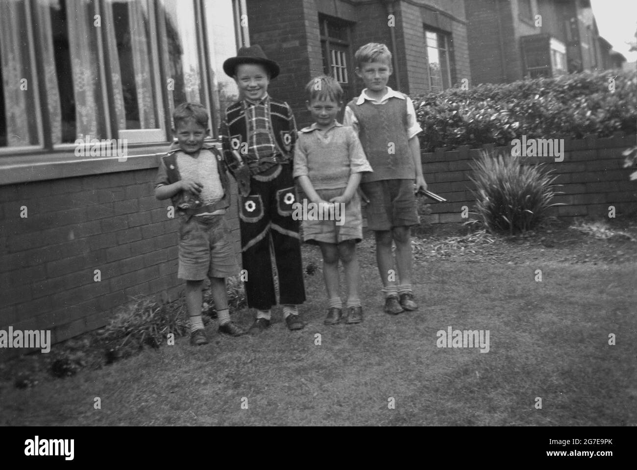 1930s, historical, four young boys standing together  in a front garden outside a house for a photo, one of the youngsters dressed in a cowboy outfit, the others all in short trousers, Mirfield, Yorkshire, England, UK. Stock Photo