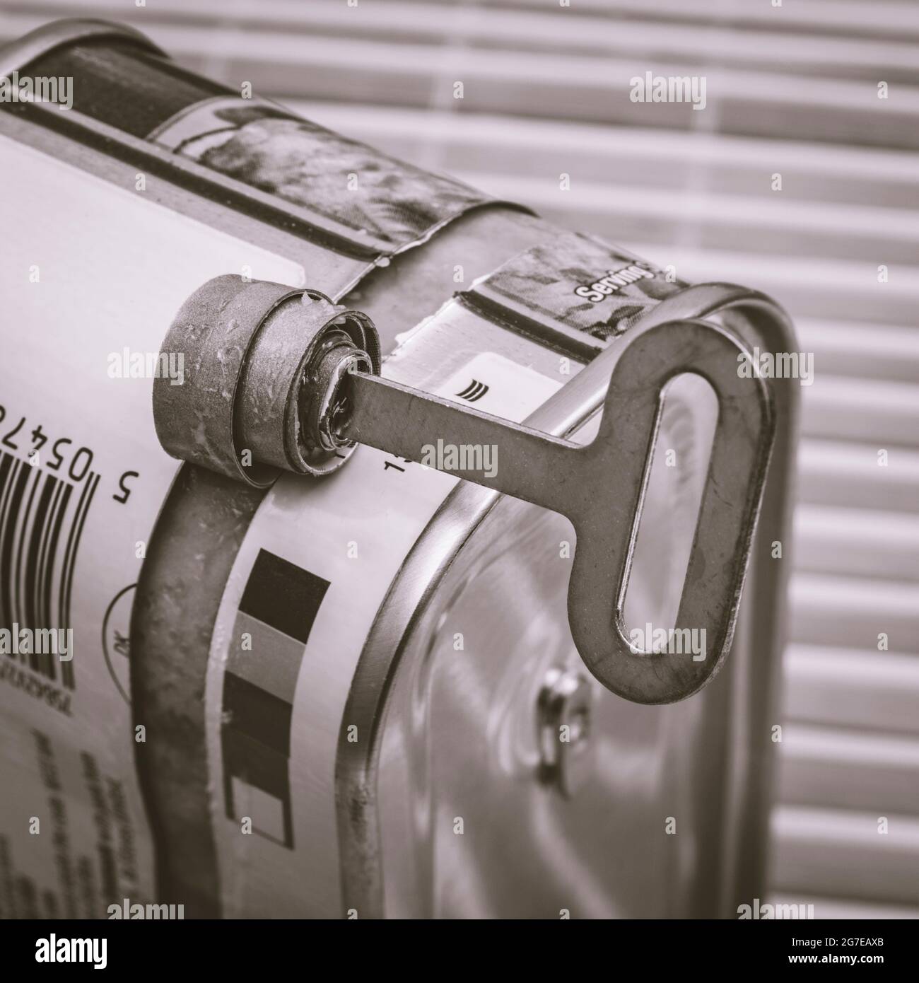 Monochrome twist-key tin opener / can-opener on an ASDA luncheon meat tinned product. Concept for food preservation, opening a can of worms. Stock Photo