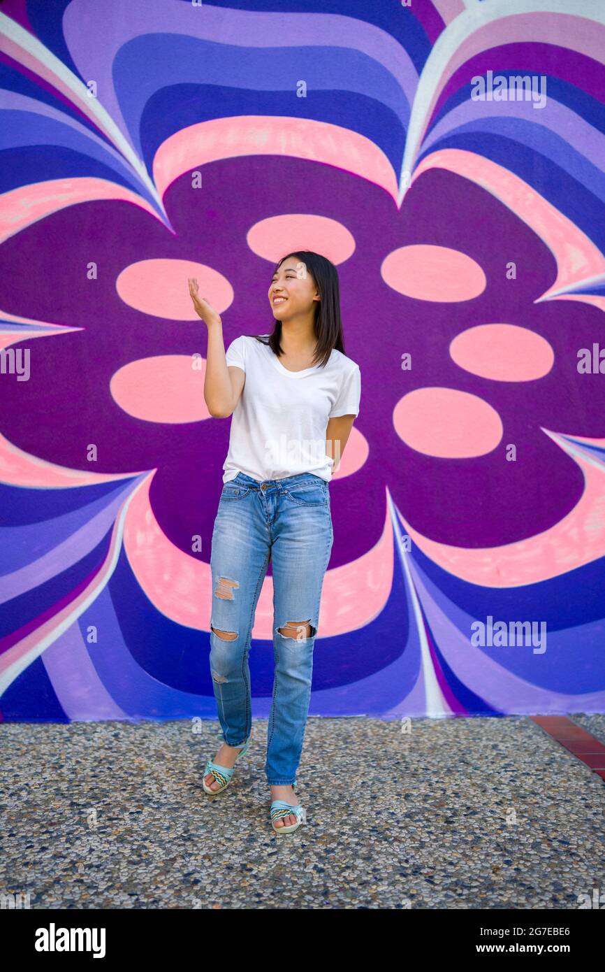Young Asian Woman in 1960s Apparel Standing in Front of 1960s Style Mural Stock Photo