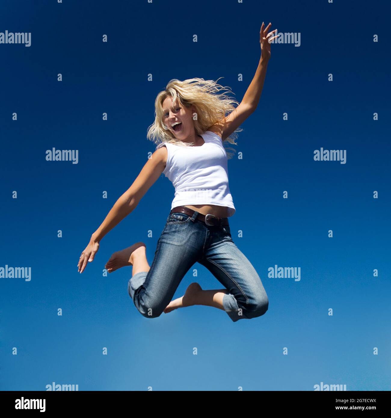 A young and beautiful woman jumping into a perfect blue sky Stock Photo ...