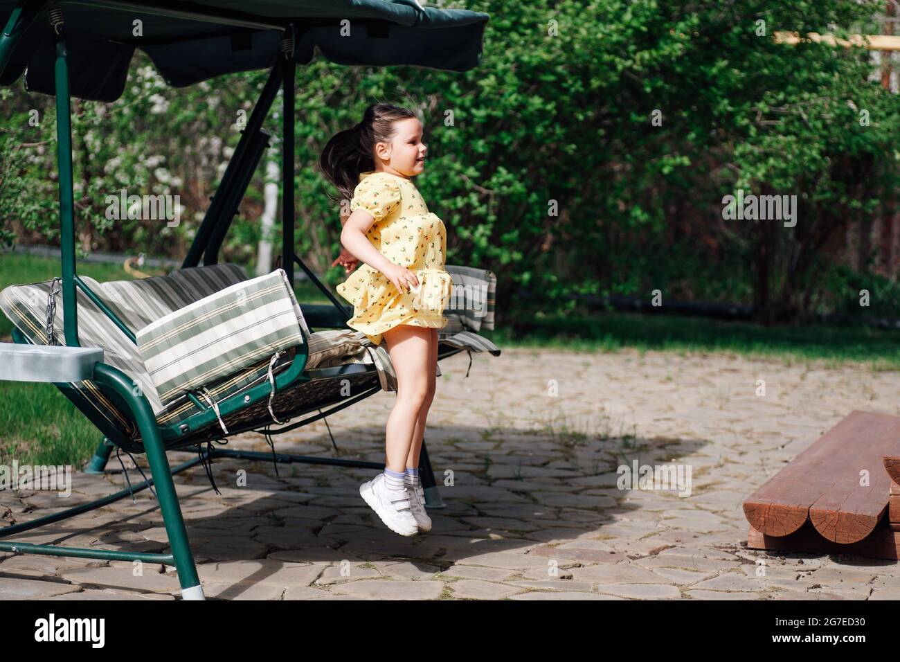 a girl jumps from a garden swing in a summer garden in the backyard, the moment of movement and flight in the air Stock Photo