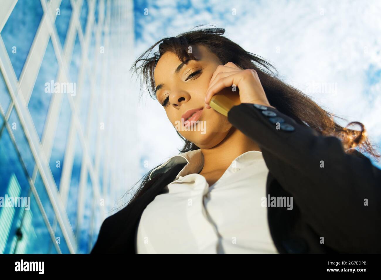 A brunette woman in business clothes using her mobile in front of a modern business building Stock Photo