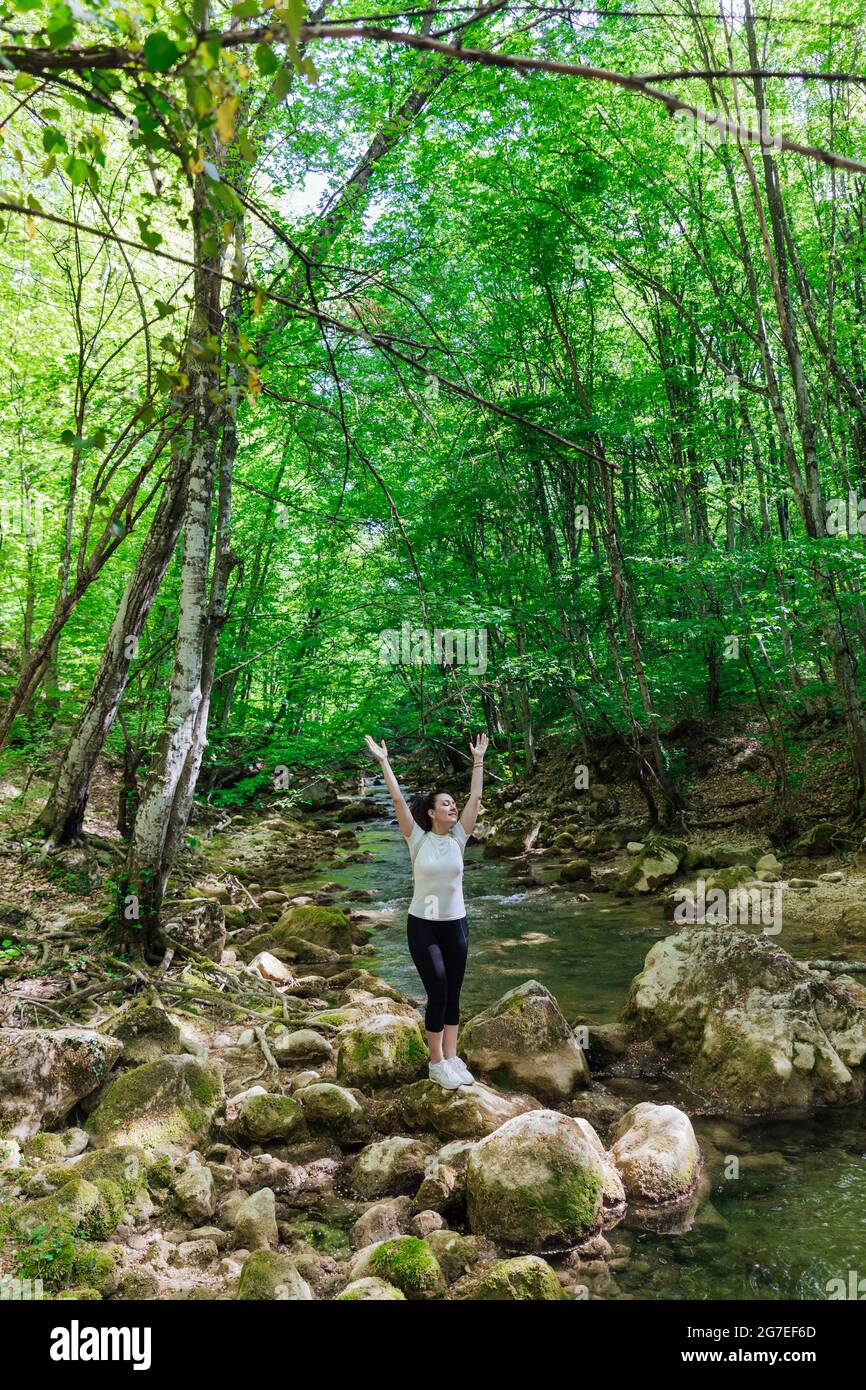 beautiful woman walking by a mountain river through a green forest ...