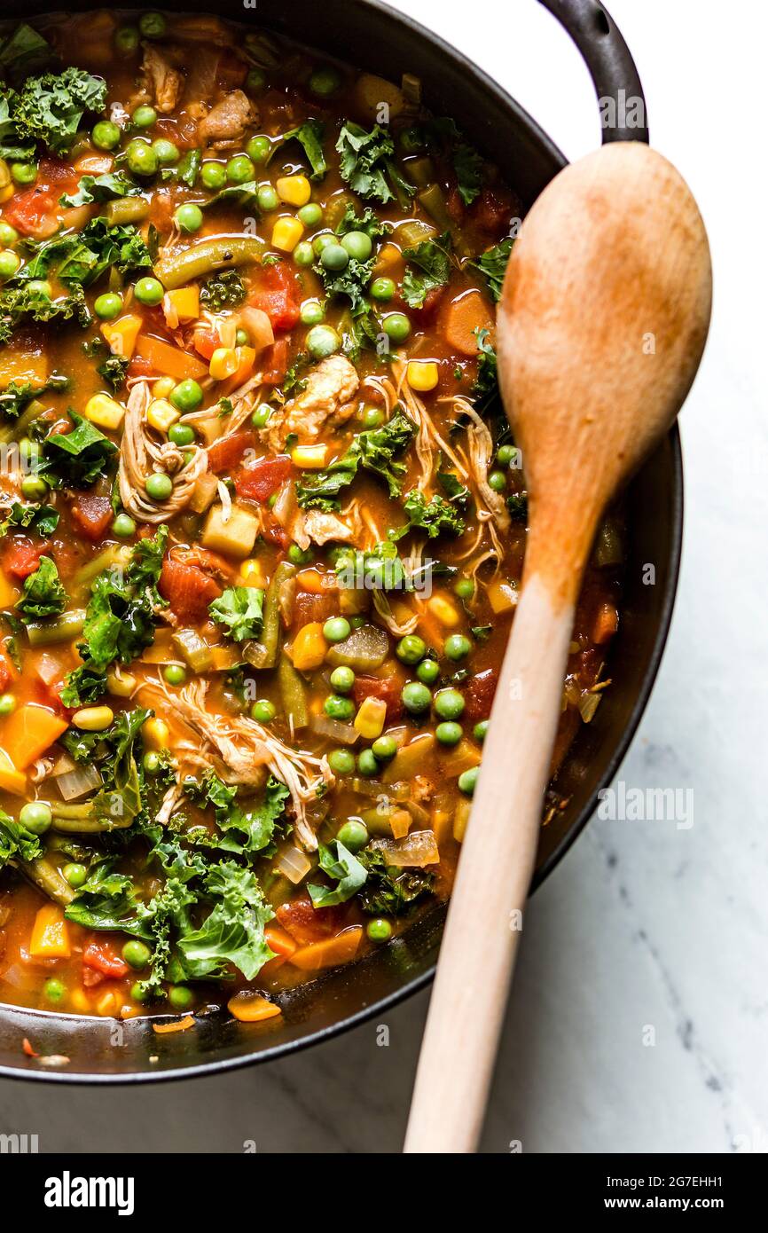 Chicken and vegeable soup being prepared in a large pan with a wooden spoon. Stock Photo