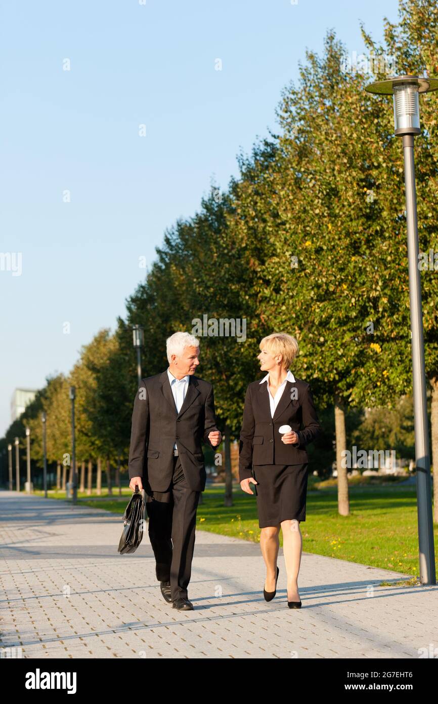 Business people - mature or senior - talking outdoors and walking in a park Stock Photo