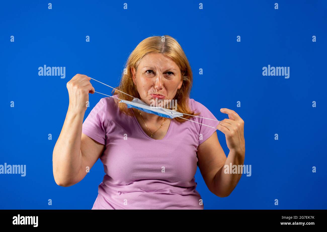 Middle blonde woman taking off her medical mask isolated on blue background Stock Photo