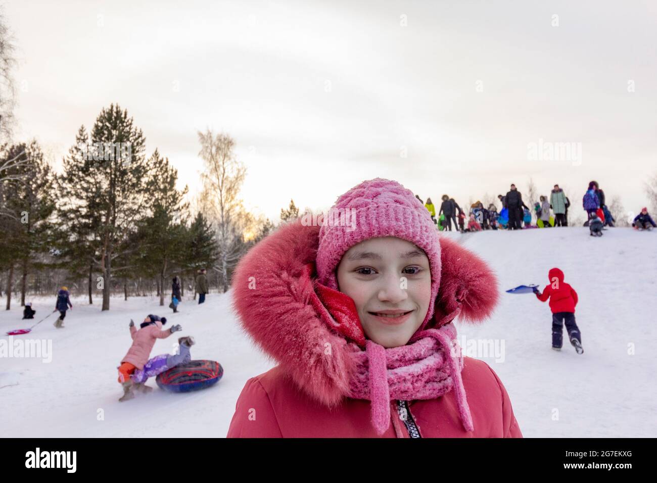 Girl with frost on the eyelashes on the background of playing children in the coldest in the world northern residential village Oymyakon. Stock Photo