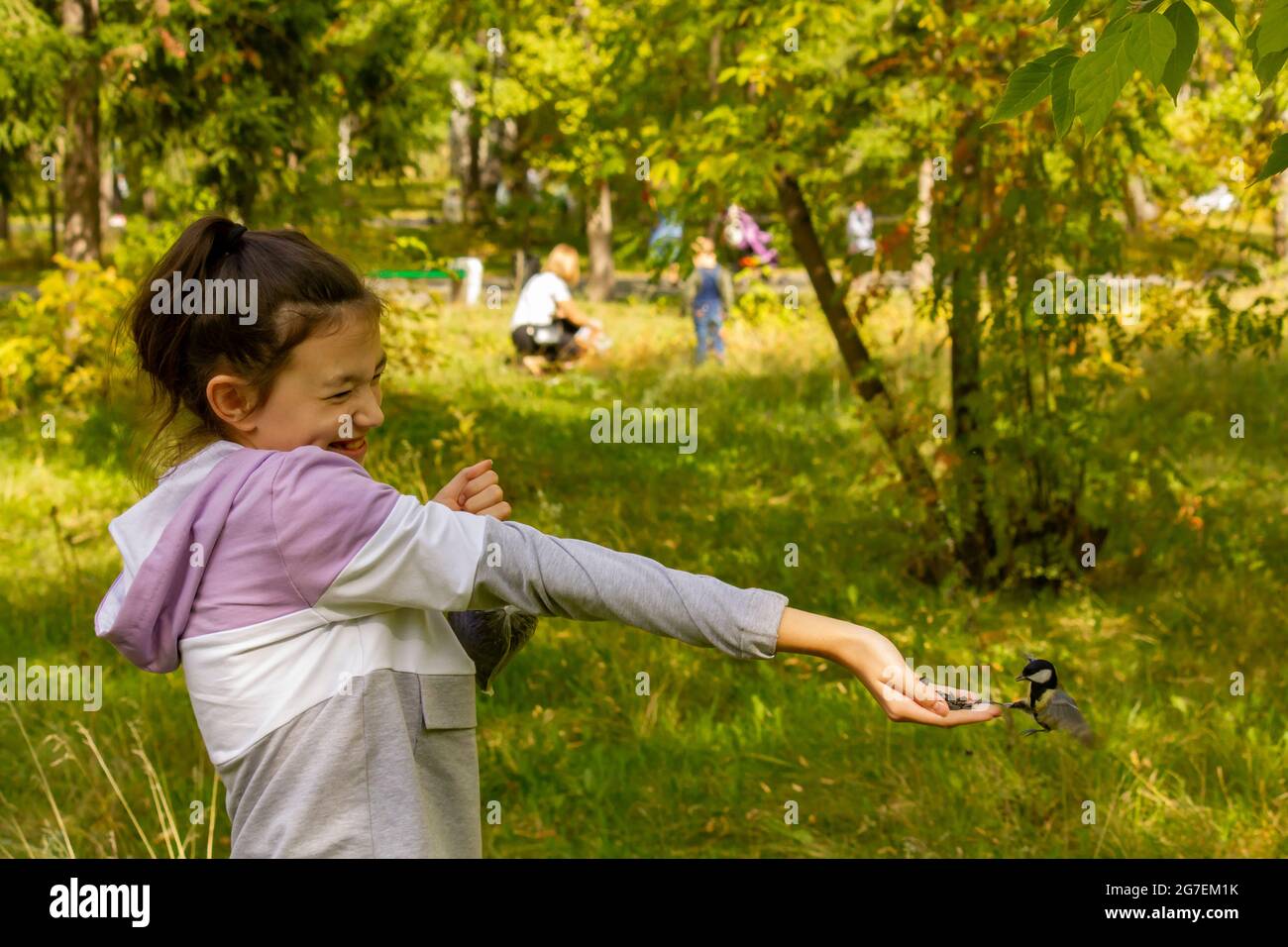 Young laughing girl feeding birds in autumn forest. The concept of spending a joint family weekend in nature. Stock Photo