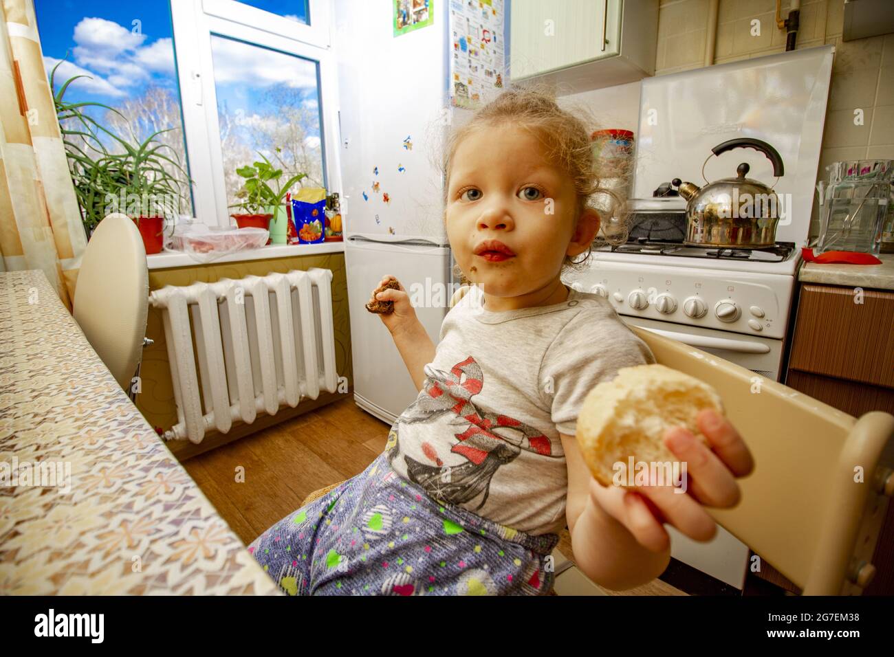 A young girl is eating dark and light bread at the same time in the kitchen. Stock Photo