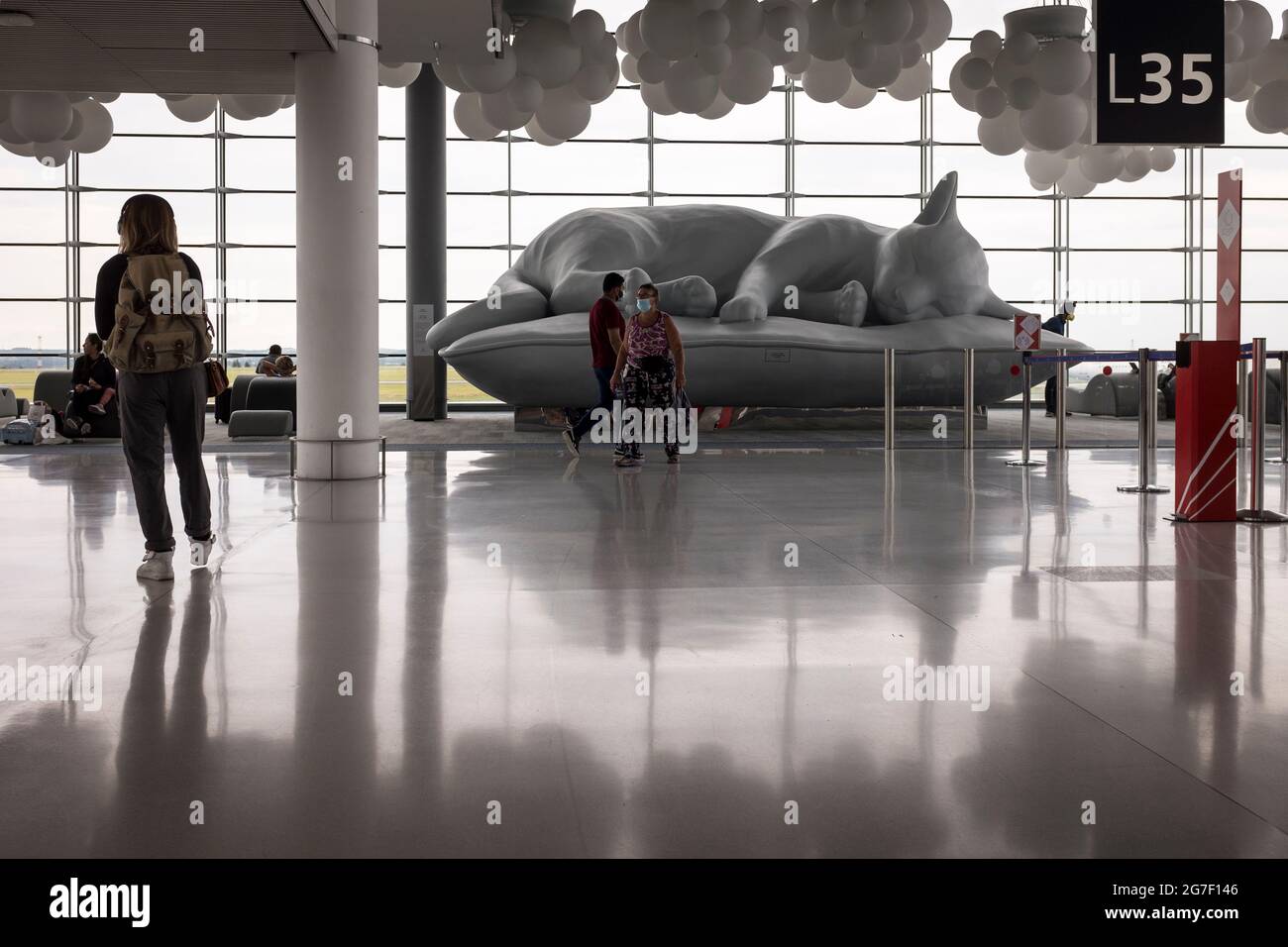 Passengers walk by a large sculpture of a reclining cat in the