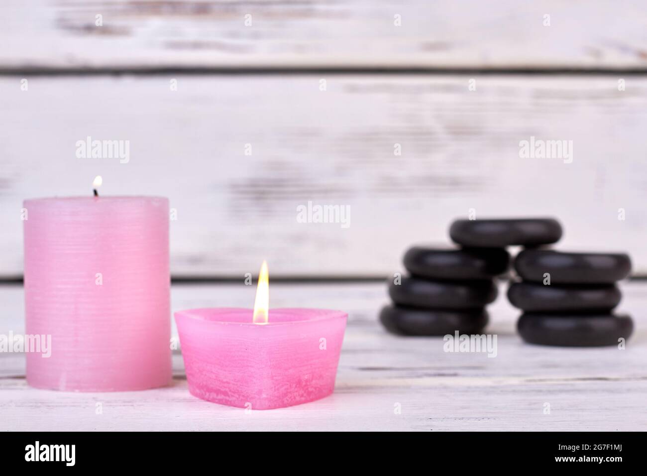 Two burning wax candles and stack of black spa stones. Stock Photo