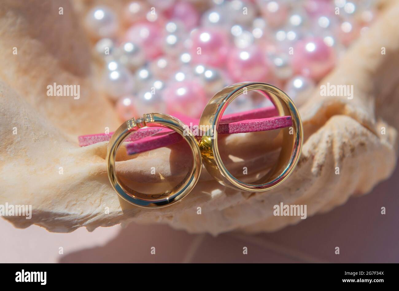Pair of gold wedding ring bands jewelry on seashell with pink and white pearl beads Stock Photo