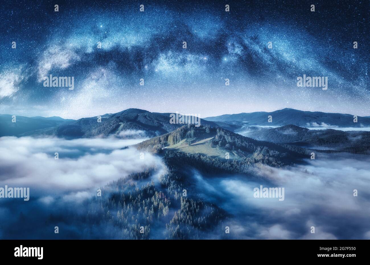 Milky Way arch and mountains in low clouds at starry night Stock Photo
