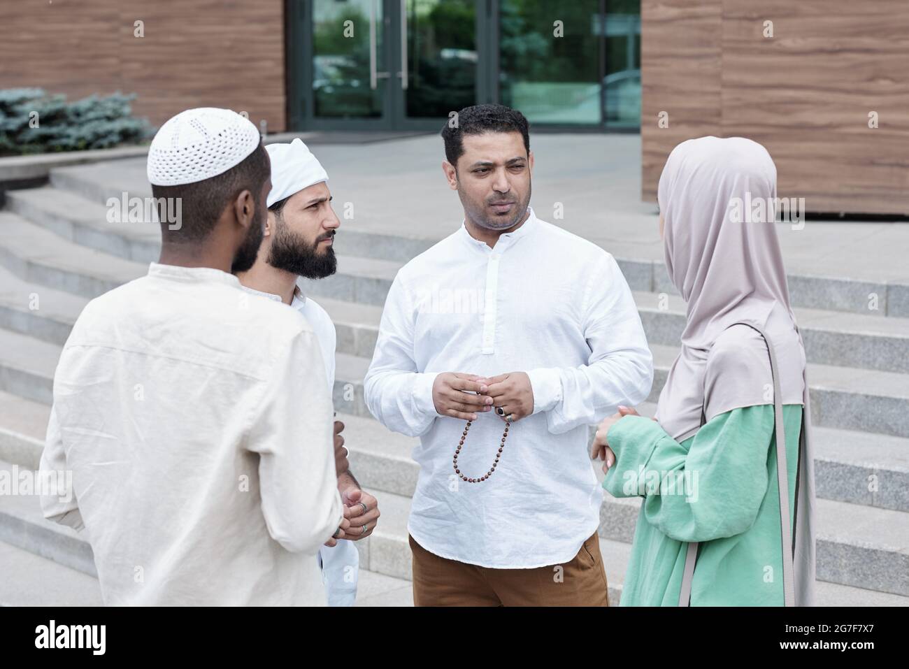 Group of thoughtful young Islamic colleagues standing against office building and brainstorming about project Stock Photo