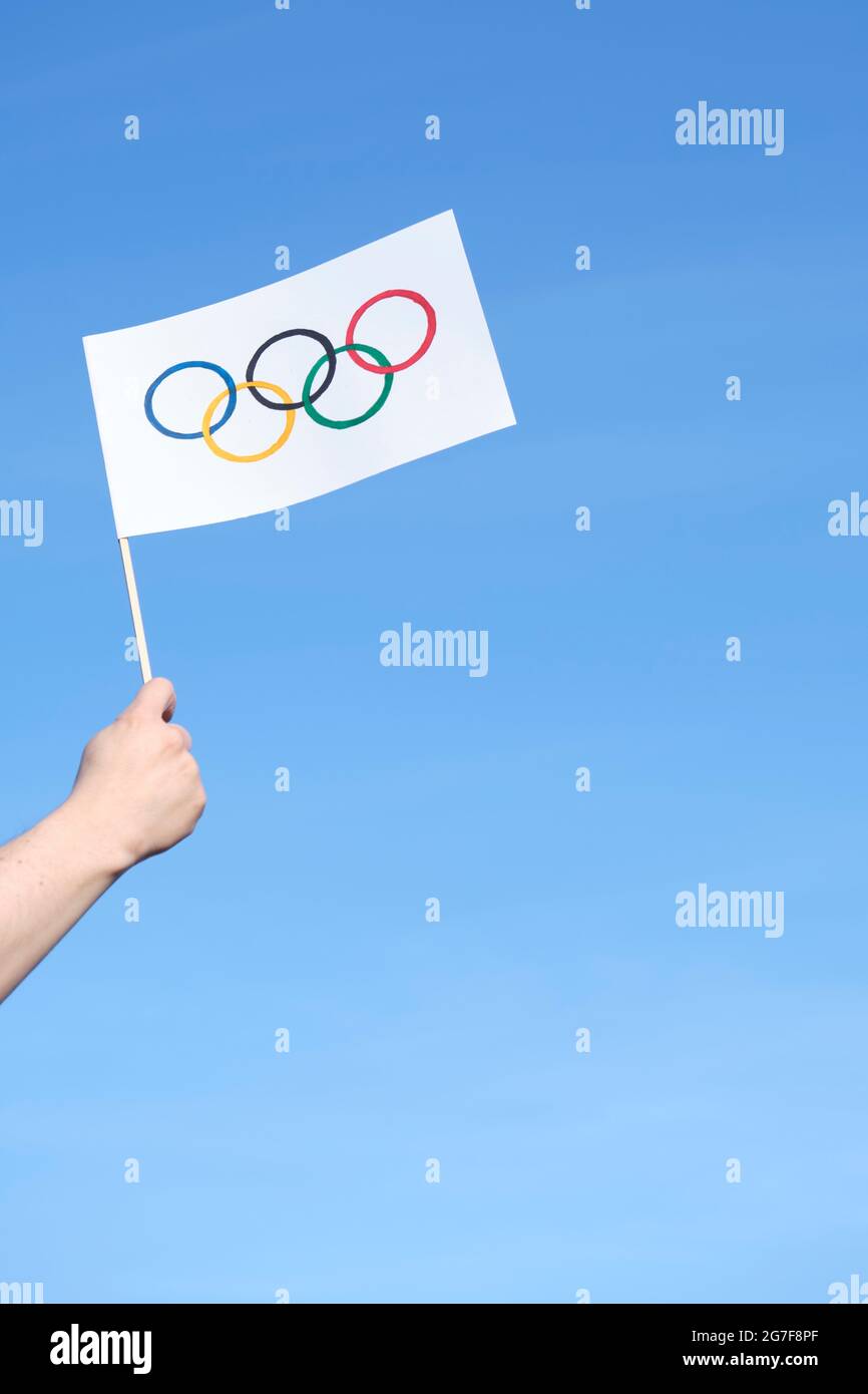 Hand holding a handmade Olympic Games flag outdoors against a clear sky on a sunny day. Image with copy space. Stock Photo