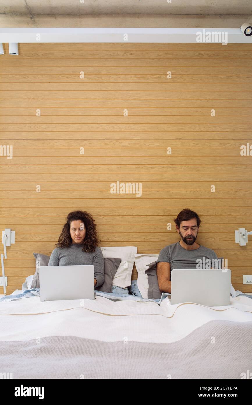 Couple in a double bed king size each with their notebook working watching each of their screens. Concept: home office Stock Photo