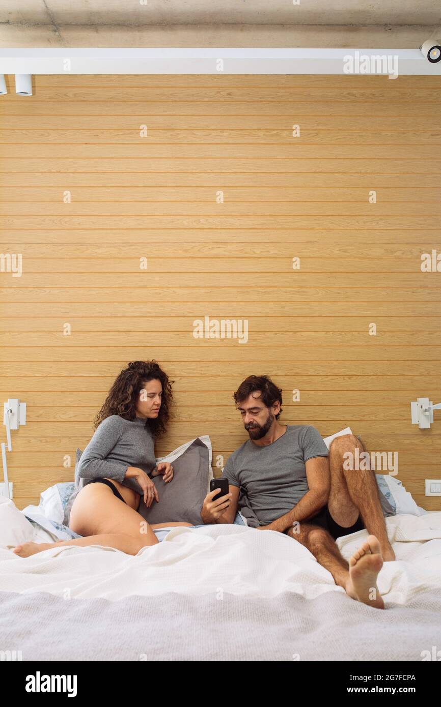Middle age couple in underpants in a double bed king size where the man is showing the woman something on his mobile phone screen Stock Photo
