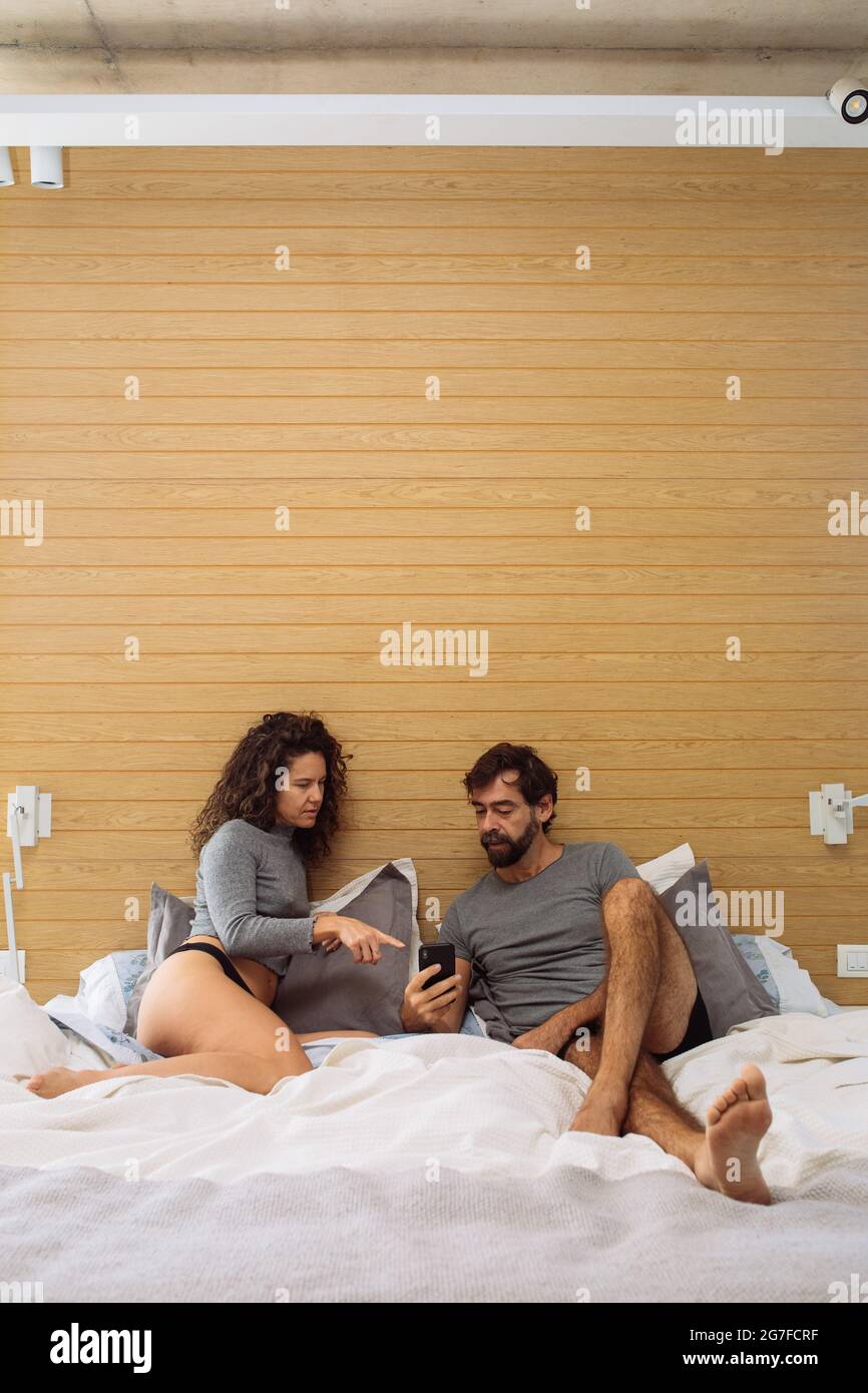 Middle age couple in underpants in a double bed king size where the girl is pointing to the man´s mobile Stock Photo