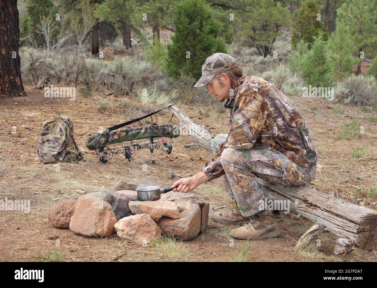 modern bowhunter sitting in camp and cooking over campfire in the woods Stock Photo