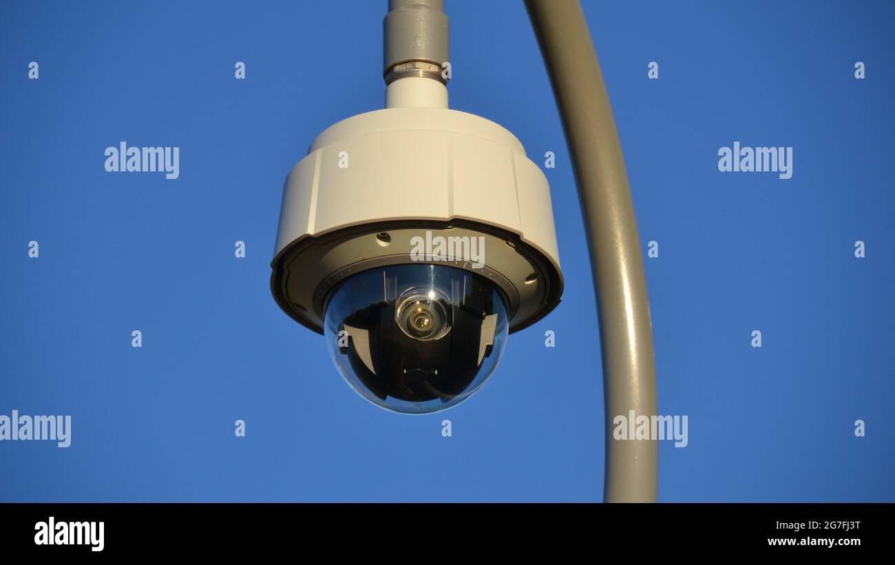 Close up view of a dome shaped CCTV or closed circuit security camera lens on a pole against a blue sky Stock Photo