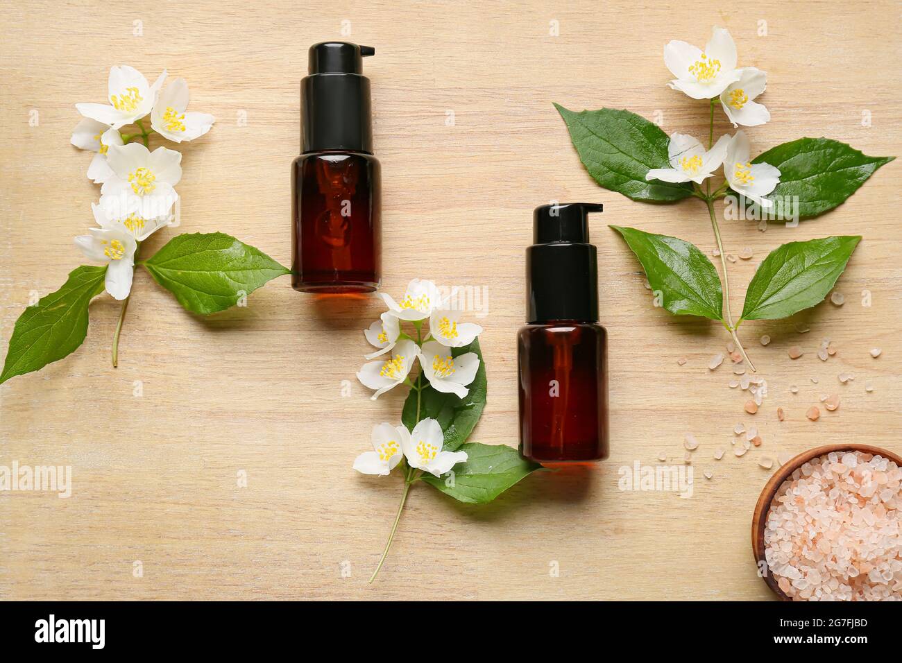 Bottles of cosmetic products, sea salt and jasmine flowers on wooden background Stock Photo