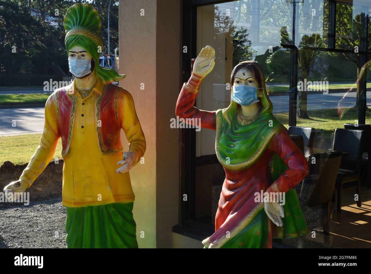Statues of a woman and a man, dressed in clothing from India and used as advertising, have Covid-19 masks placed over their faces outside an Indian fo Stock Photo