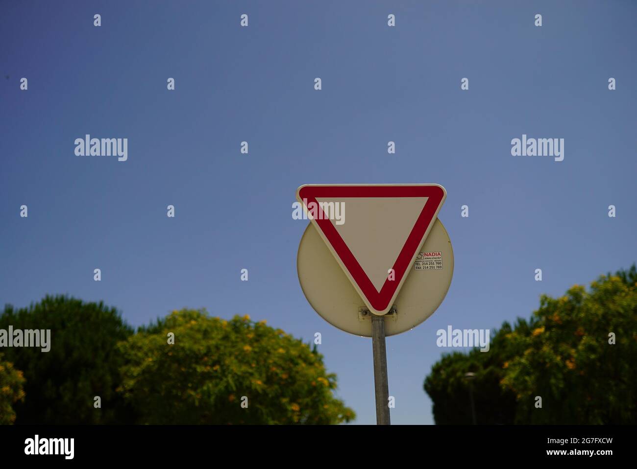 Triangular red-outlined banning roadsign on blue background Stock Photo