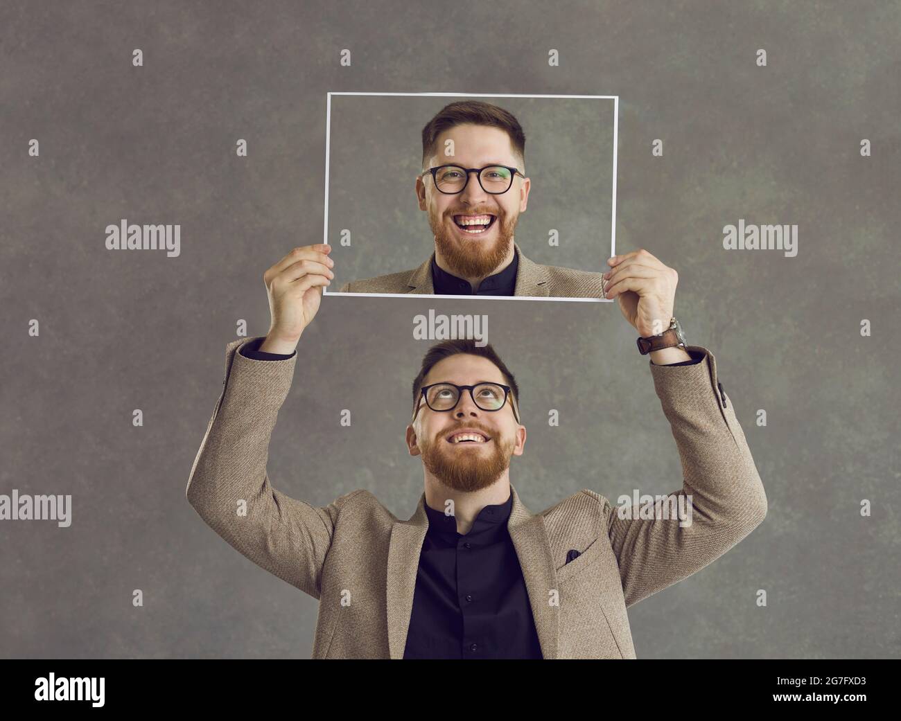 Happy smiling man holding a photo of himself laughing isolated on a grey background Stock Photo