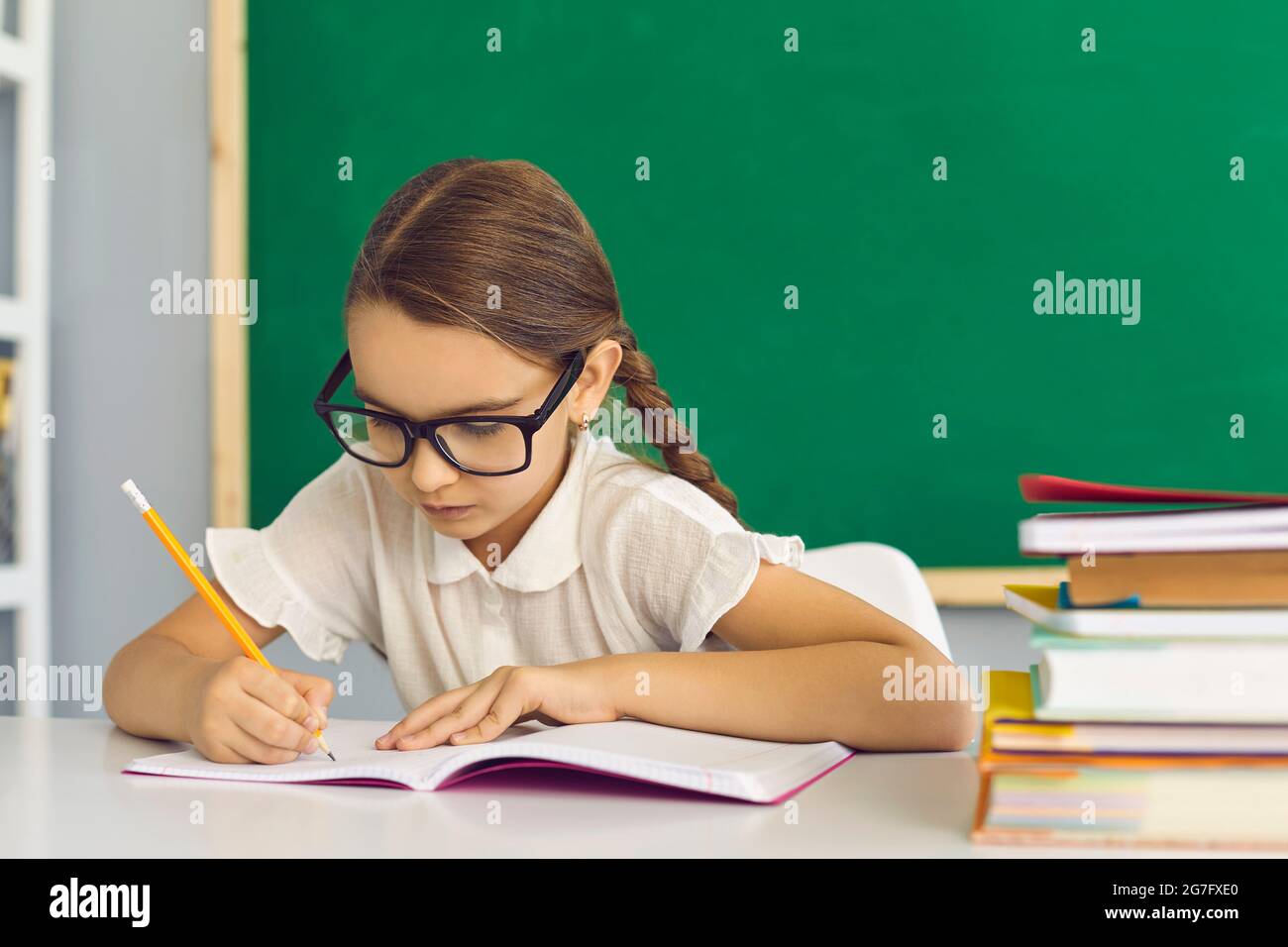 Little student girl sitting at desk in classroom and writing in her ...