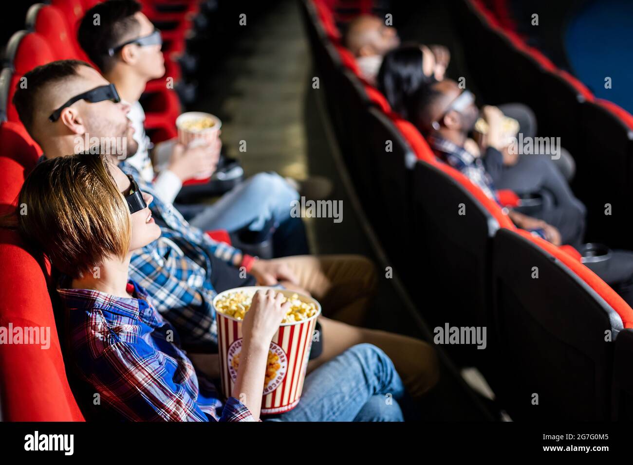 Friends are watching a movie in the cinema. People sit in the armchairs of the cinema and look at the screen with special glasses for 3D Stock Photo