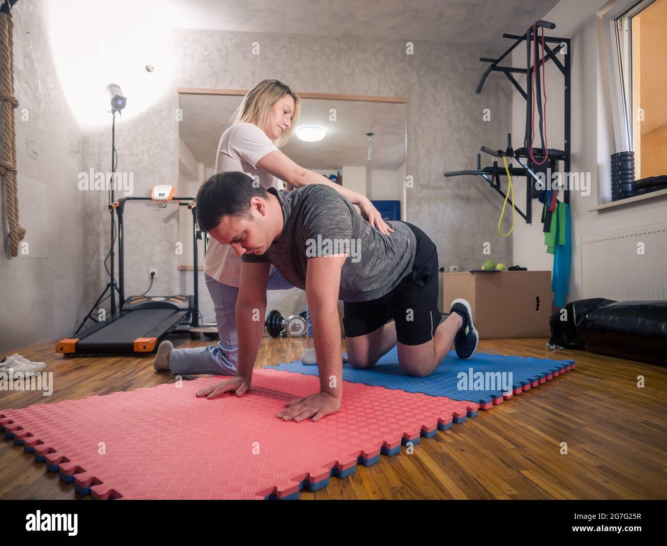 Physiotherapy indoors in a room. One young adult man exercising back muscles and working out with young woman therapist. Stock Photo