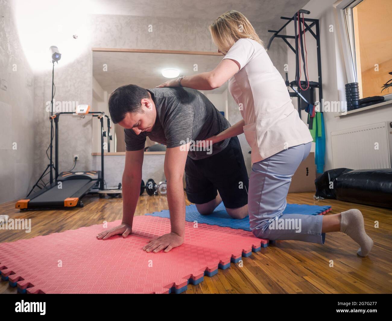 Physiotherapy indoors in a room. One young adult man exercising abdominal and working out with young woman therapist. Stock Photo