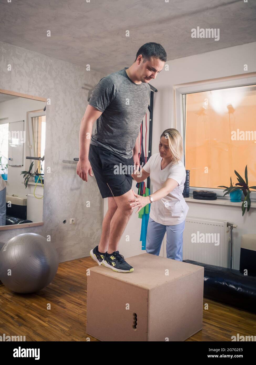 Physiotherapy indoors in a room. One young adult man exercising knee and working out with young woman therapist. Stock Photo