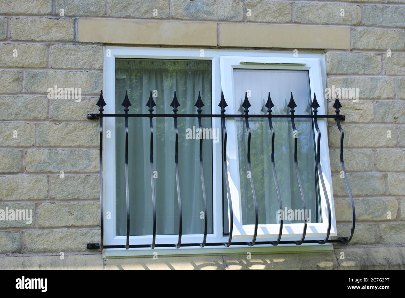 Double glazing white UPVC window frame with wrought iron security railings set into sandstone block wall Stock Photo