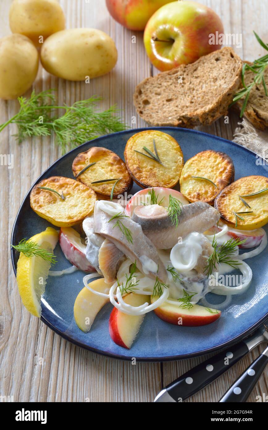 Salty herring fillets with apple slices and sour cream sauce, served with crispy baked rosemary potatoes Stock Photo