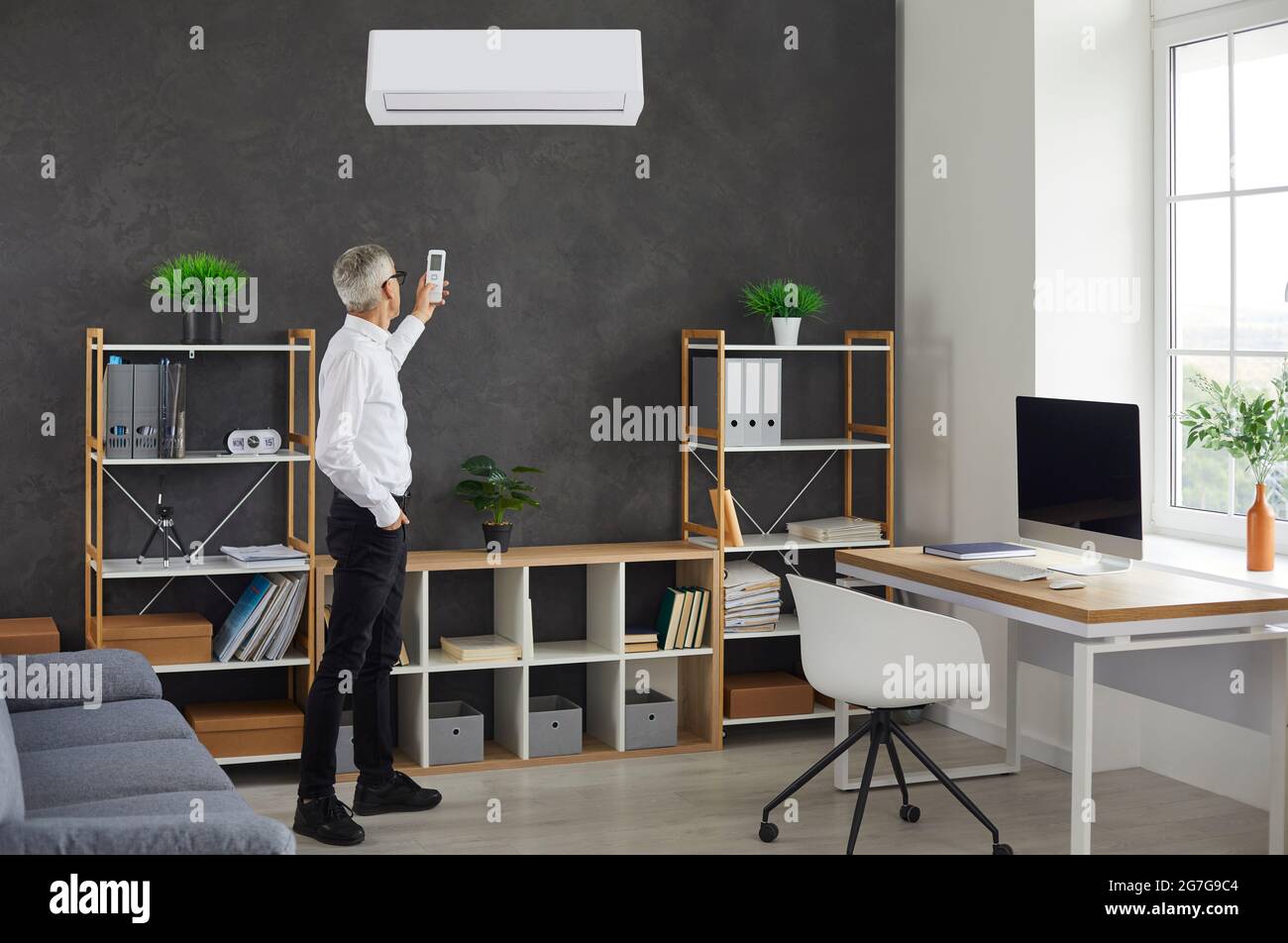 Businessman switching a modern wall mounted air conditioner in his office at work Stock Photo