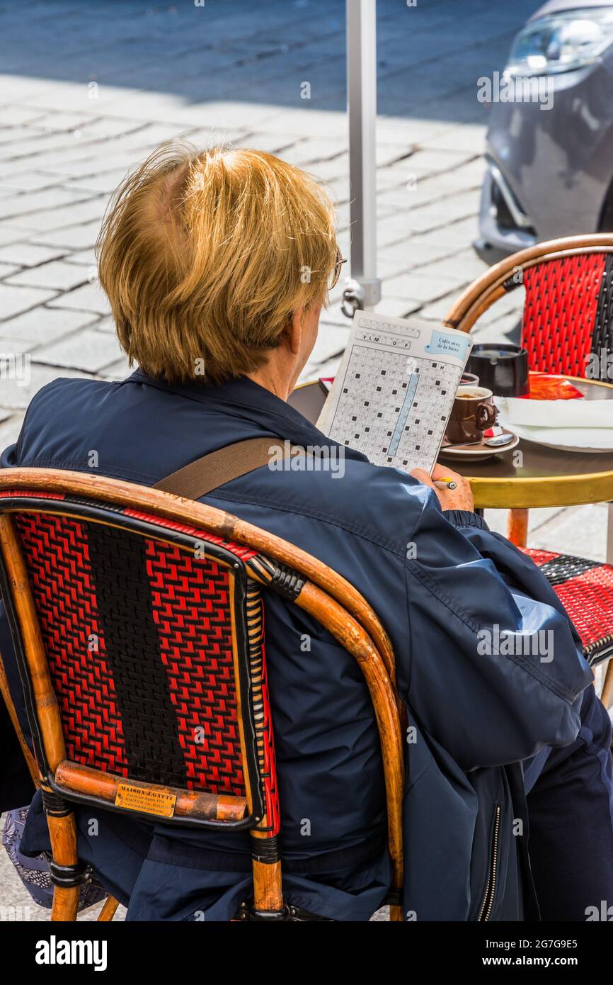 Woman sat at outdoor table doing crossword puzzle - Paris, France. Stock Photo